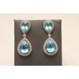 A PAIR OF BLUE TOPAZ AND DIAMOND CLUSTER DROP EAR STUDS, the faceted tear cut topaz claw set to an