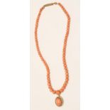 A CORAL NECKLACE, the single string of graduated beads hung with an oval pendant centrally claw
