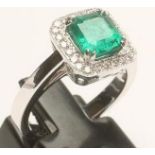 AN EMERALD AND DIAMOND CLUSTER RING, the Colombian square cut emerald claw set to a border of