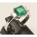 AN EMERALD AND DIAMOND THREE STONE RING, the square cut emerald claw set and flanked by two baguette
