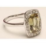 A YELLOW SAPPHIRE AND DIAMOND RING, the mixed cushion cut sapphire claw set to a border of