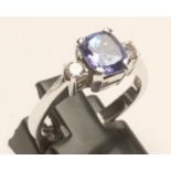 A TANZANITE AND DIAMOND THREE STONE RING, the princess cut tanzanite claw set and flanked by two