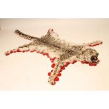 A SNOW LEOPARD SKIN RUG, with snarling head, glass eyes, mounted on cloth with a red felt edging,