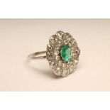 AN EMERALD AND DIAMOND FLOWERHEAD RING, the central facet cut emerald claw set to a double border of