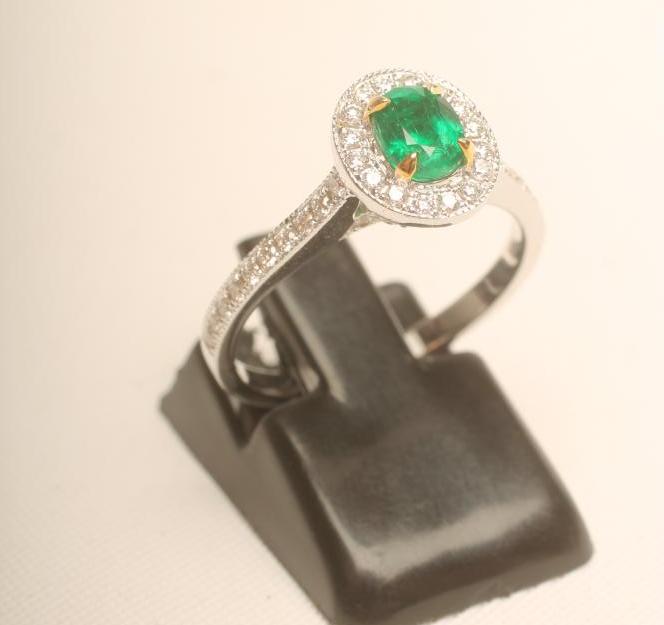 AN EMERALD AND DIAMOND CLUSTER RING, the oval facet cut Columbian emerald claw set to a border of