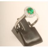 AN EMERALD AND DIAMOND CLUSTER RING, the oval facet cut Columbian emerald claw set to a border of