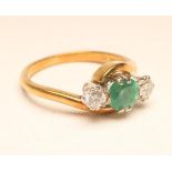 A THREE STONE EMERALD AND DIAMOND RING, the central round cut emerald claw set and flanked by two