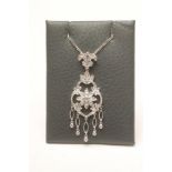 A DIAMOND PENDANT, the open lozenge panel centred by a flowerhead and hung with five "tassels"
