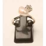 A BAROQUE PEARL AND DIAMOND RING, the pearl drilled and set beside a triple cluster of small