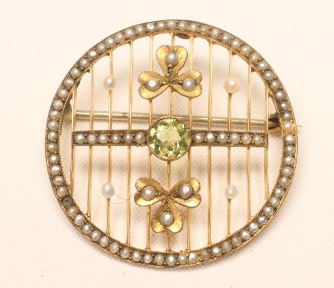 AN EDWARDIAN CIRCULAR BROOCH, centred by an open back collet set peridot flanked by two seed pearl