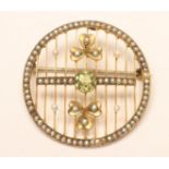 AN EDWARDIAN CIRCULAR BROOCH, centred by an open back collet set peridot flanked by two seed pearl