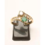 AN EMERALD AND DIAMOND CROSSOVER RING, claw set with an emerald and diamond to pave diamond set