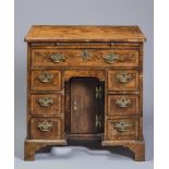 AN EARLY GEORGIAN SMALL WALNUT KNEEHOLE DESK, the rounded oblong top quarter veneered with feather