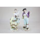 A pair of Dresden porcelain figures of a male musician and a female dancer, standing on scroll