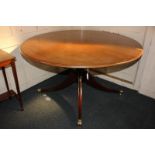 A mahogany circular dining table on turned pedestal support, with four curved legs capped with brass