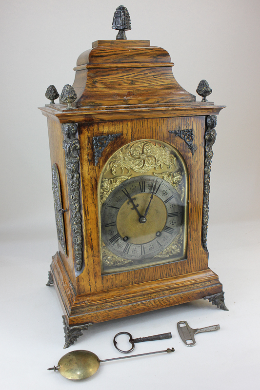 A gilt metal mounted oak mantel clock with arched brass dial, with silvered chapter ring, movement