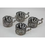 A set of four late Victorian silver cup holders decorated with cherubs amongst pierced and scroll