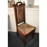 An Arts and Crafts oak rush seated dining chair with slatted back