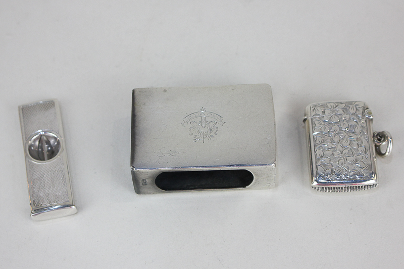 An Elizabeth II silver cigar cutter, a silver vesta case, and a white metal matchbox cover