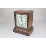 An early 20th century oak cased mantel clock, the square enamelled dial with Roman numerals, the