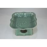 A Chinese green celadon pottery dish on stand depicting two birds on a branch, with flowering and