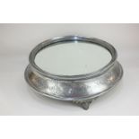 A large silver plated cake stand with mirrored surface, the sides with chased scrolling design, on