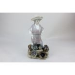 A Lladro porcelain figure of a young lady in hat and poncho, standing before a display of pots and