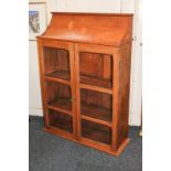 A pine wall cupboard with sloping top, twin glazed panel doors (one glass panel missing) enclosing