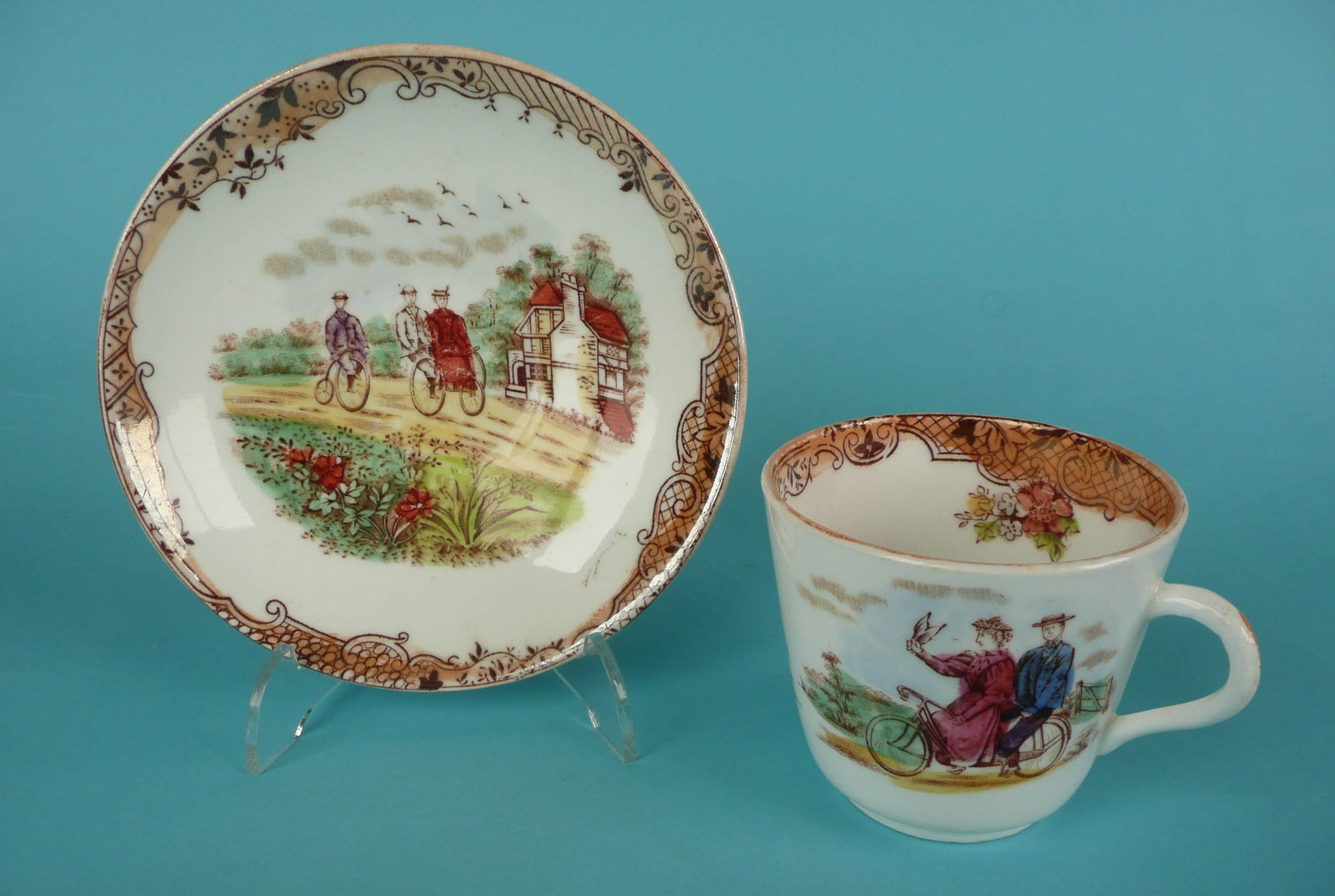 Cycling: a porcelain cup and saucer printed in brown and decorated in colours with cycling scenes,