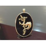 DRAGON PENDANT MOUNTED ON A BLACK HARDSTONE WITH 14K MARKED FRAME AND HANGER.