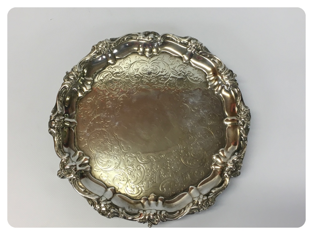 A WHITE METAL PIE CRUST EDGE SALVER WITH SCROLL AND FLOWER RIM, ON TRIPOD SCROLLED FEET,