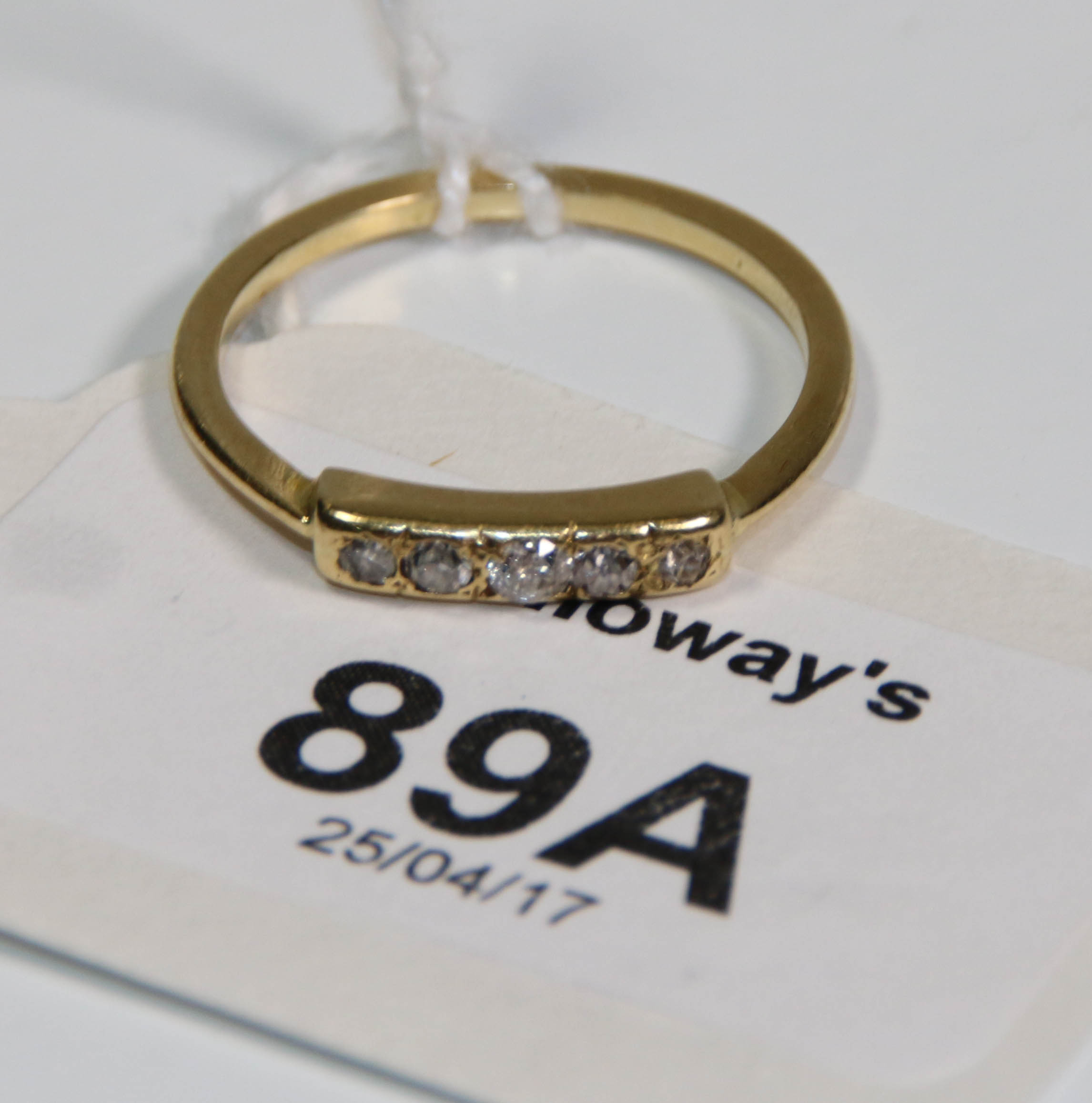 A yellow metal engagement ring, set with five small diamonds to a bar