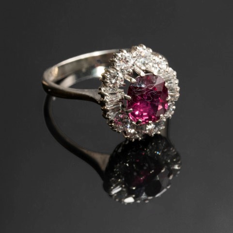 A ruby and diamond cluster ring, the oval cut ruby in raised claw mount, within a border of