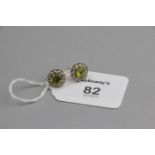 A pair of peridot and diamond cluster earrings, the circular cut peridots, claw mounted within a