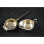 A miniature silver cream jug, London 1908, together with a silver tea strainer with wooden handle