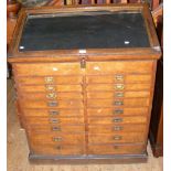A Victorian oak shop cabinet with sloping glazed top and multiple drawers below having sunken