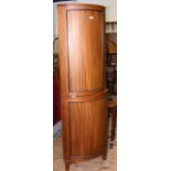 A mahogany bow-front corner cabinet enclosed by panelled doors