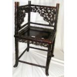 An ornately carved Chinese hardwood corner chair with pierced prunus decoration to the back rest