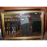 A 78cm x 109cm hanging bevelled wall mirror in ebonized and gilt frame