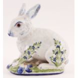 A DELFT STYLE GLAZED SEATED RABBIT with amber eyes and decorated flower spray decoration, the