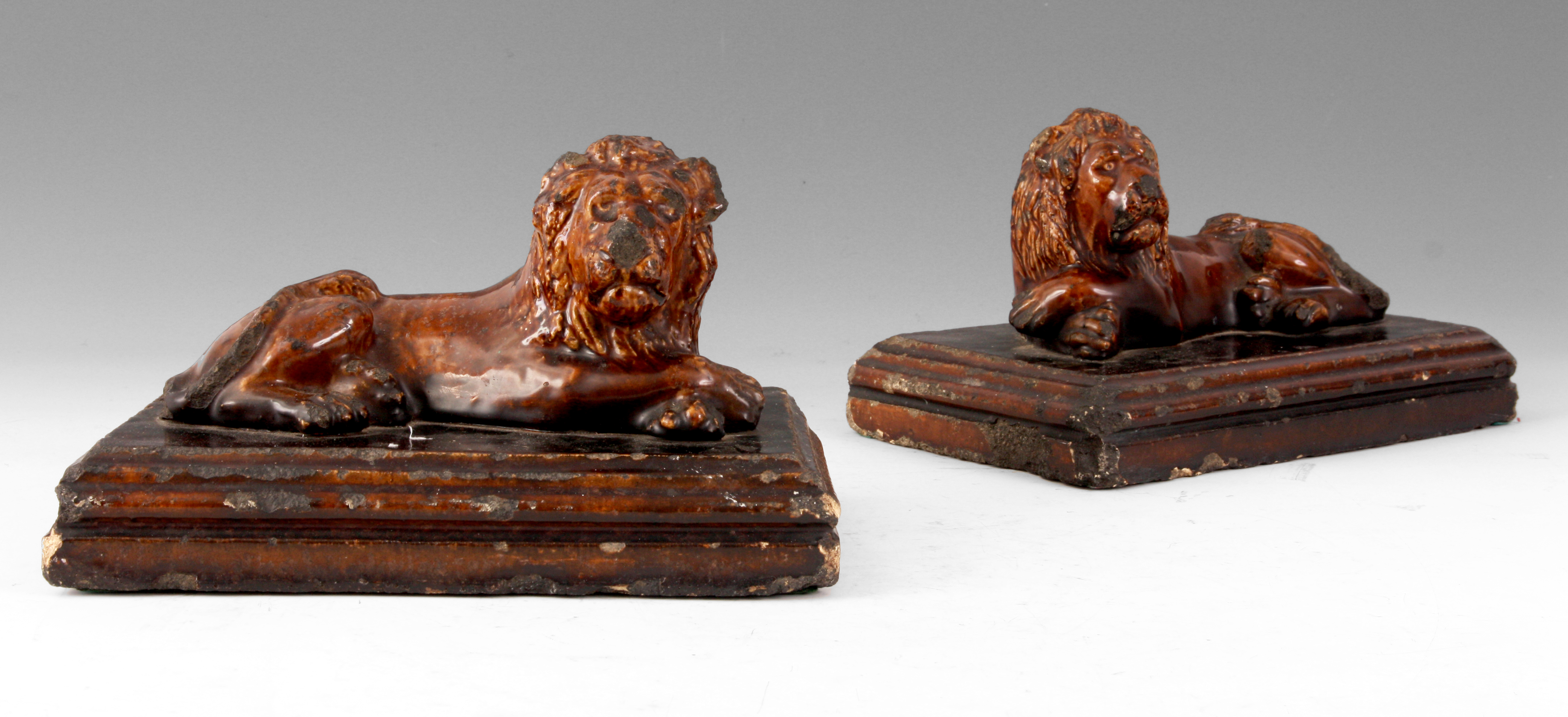 A PAIR OF 19TH CENTURY TREACLE GLAZED STAFFORDSHIRE RECUMBENT LIONS on moulded plinth bases 25cm
