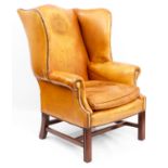 A GEORGE III STYLE MAHOGANY FRAMED LIGHT TANNED LEATHER WINGBACK ARMCHAIR with shaped back and