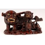 A CHINESE CARVED HARDWOOD FOO DOG FIGURE with young Foo dog having bone eyes and teeth on leaf