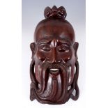 AN ORIENTAL CARVED HARDWOOD MASK OF A DEITY having bone inlaid eyes and teeth 49cm overall