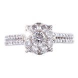 AN 18ct WHITE GOLD SEVEN STONE CLUSTER DIAMOND RING having double row diamond set shoulders, 1 carat