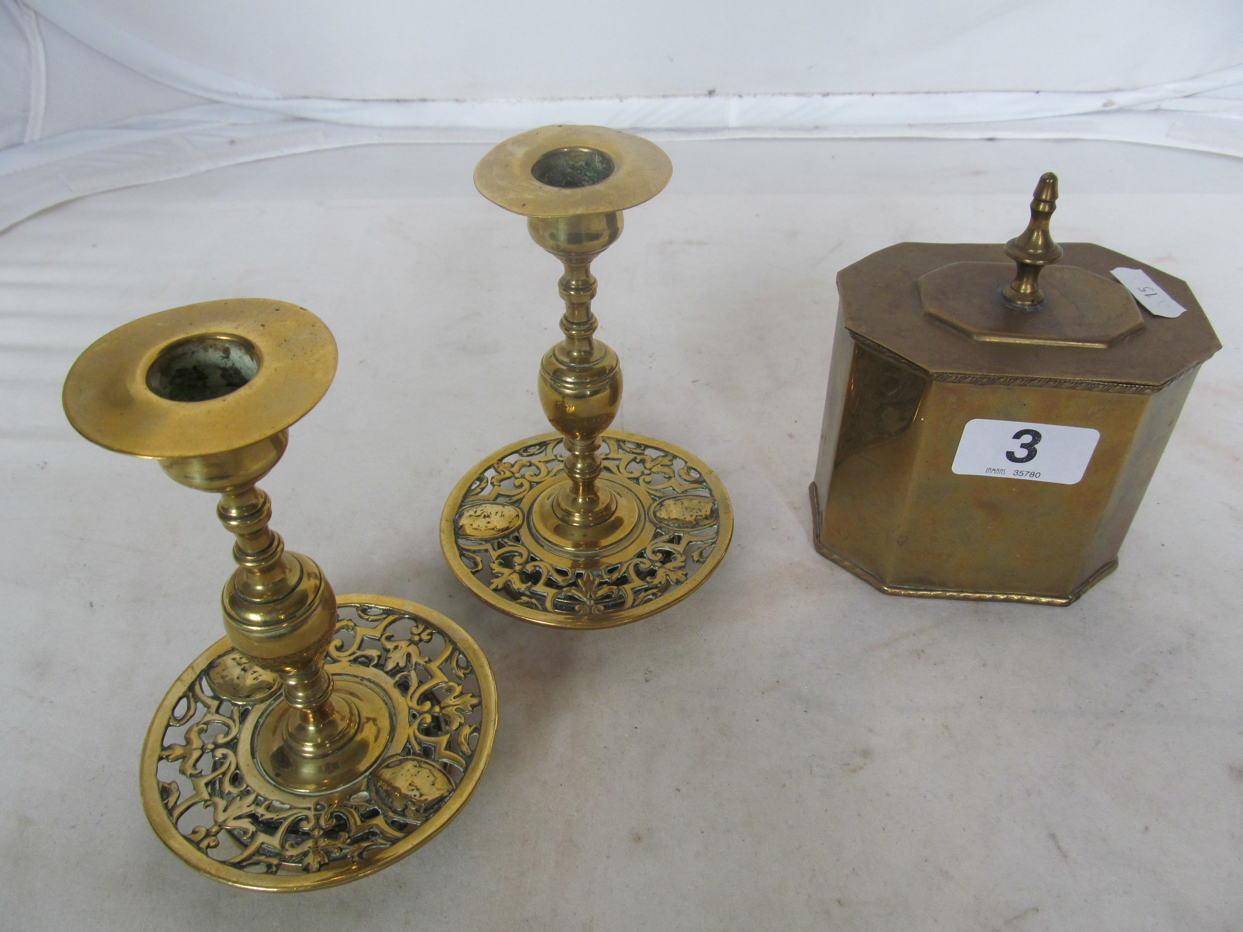 A brass tea caddy and a pair of brass candlesticks with pierced sconces