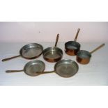 Six assorted copper pans with brass handles.