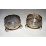 A pair of sterling silver salts, each intricately etched and standing on three bun feet,