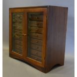 A Hardwood Collectors' Cabinet with two glazed doors enclosing eighteen drawers with knob handles,