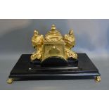 A French Brass and Ebonised Inkstand in the Empire Style with figural mounts raised upon low brass